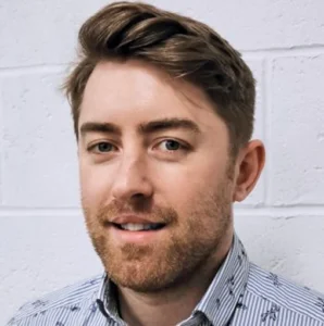 Connor Doughty - A headshot of the Director, Connor Doughty against a white brick wall.